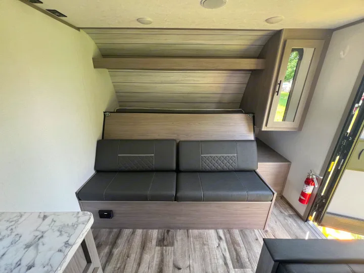 RV rental interior: gray sofa/dinette, upper bunk bed, wood-look panels, and marble table, with safety equipment visible.. Coleman Lantern 18 2024