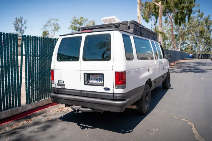 White Ford Econoline van, likely an RV rental, equipped with a roof rack & vent, parked by a fence in California. Ready for adventure.. Ford Econoline 2008