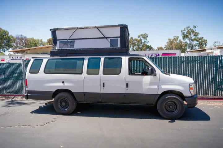 White pop-top camper van, a great RV rental. Side view shows raised roof tent, black lower body, and rugged tires.. Ford Econoline 2008