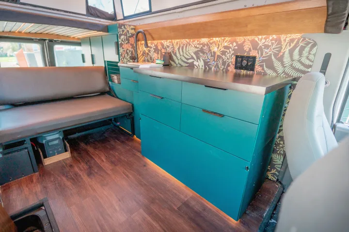 Inside a modern RV rental: teal kitchenette with botanical backsplash, wood floors, and comfy bench seating.. Ford Econoline 2008