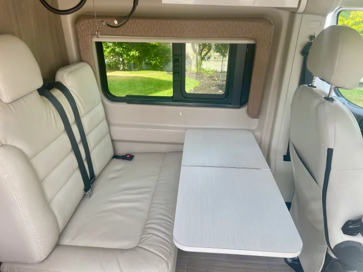 Interior of an RV rental with light-colored seating, a flexible table, and scenic window views for your journey.. Thor Tellaro 2022