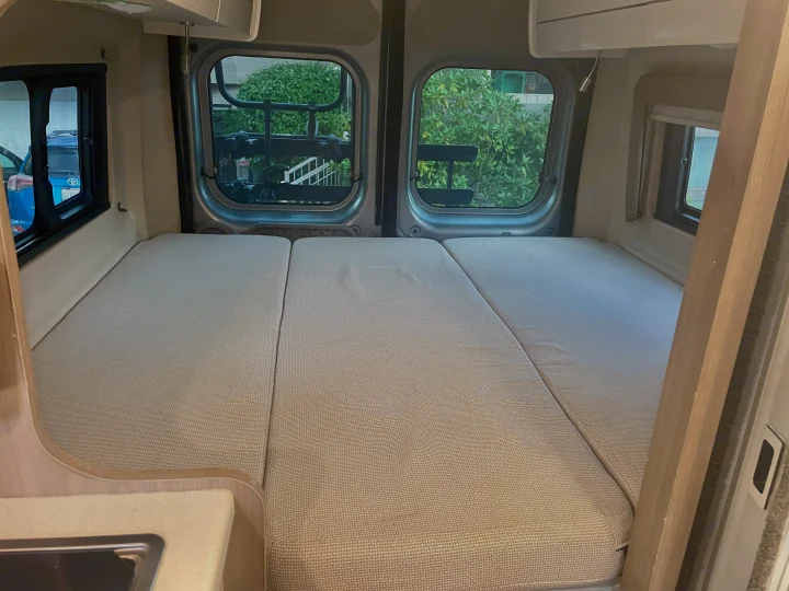 Inside a cozy rv rental: A modular bed with three segments, large windows, and a small sink area visible.. Thor Tellaro 2022
