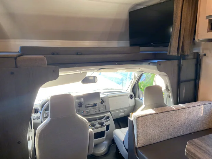 RV rental interior: cockpit, over-cab bunk, TV, and dining area in a spacious camper.. Forest River Solera 2023