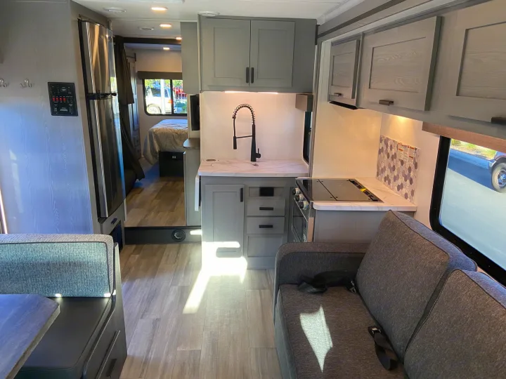 Interior of a modern rv rental, featuring a full kitchenette with grey cabinets & stainless fridge, dining booth, and bedroom. Bright & functional design.. Forest River Solera 2023