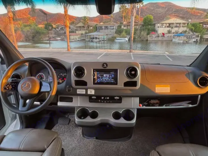RV rental interior: Mercedes-Benz Sprinter dashboard with a stunning lake, houses & mountain view.. Thor Quantum 2019