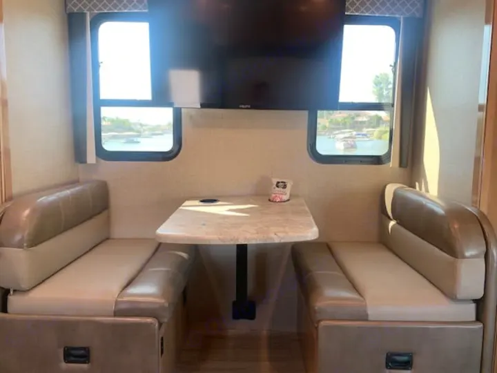 RV rental dinette featuring two benches, a table, and TV. Enjoy a water view with boats through the windows.. Thor Quantum 2019