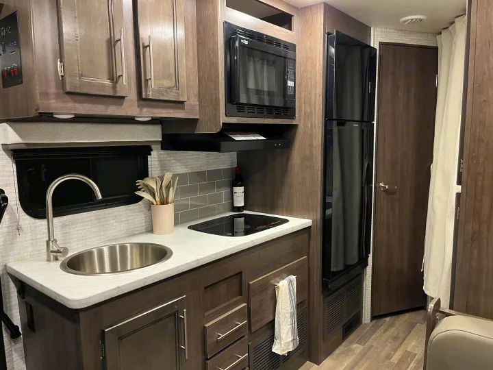 RV rental: Compact kitchen featuring a sink, stovetop, microwave, and large fridge, ready for your road trips.. Entegra Odyssey SE 2025
