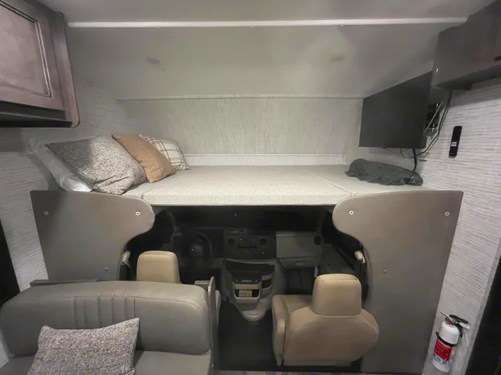 Inside an RV rental: cab-over bunk with pillows, TV, front cabin seating, and fire extinguisher.. Entegra Odyssey SE 2025
