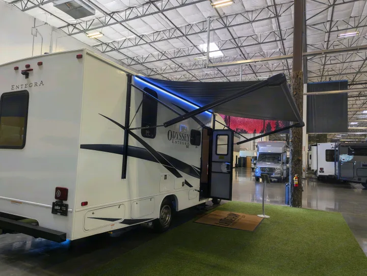 A modern Entegra RV is shown indoors on artificial grass with its illuminated awning extended, ideal for an rv rental.. Entegra Odyssey SE 2025
