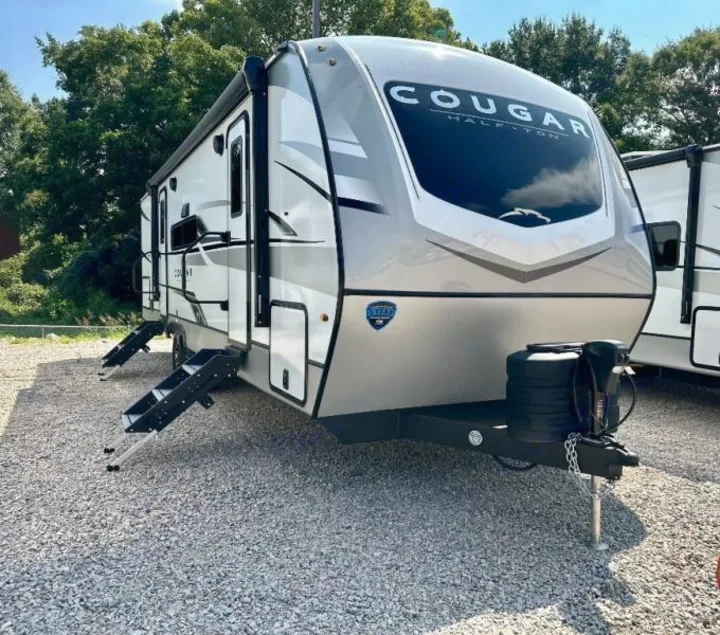 A new Cougar Half-Ton travel trailer, great for an rv rental. This modern towable RV is seen on a gravel lot with steps down.. Keystone RV Cougar 2024