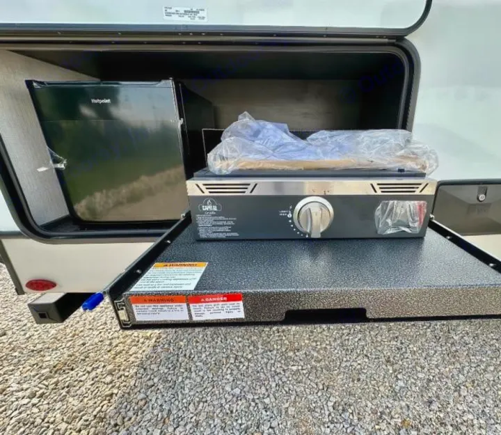 RV rental outdoor kitchen featuring a Hotpoint fridge and a Capital Griddle in an open storage compartment.. Keystone RV Cougar 2024