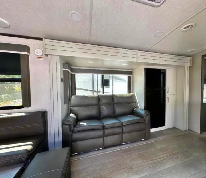 RV rental: Modern living space with gray reclining sofa, dining booth, and full-size fridge. Bright interior for adventures.. Keystone RV Cougar 2024