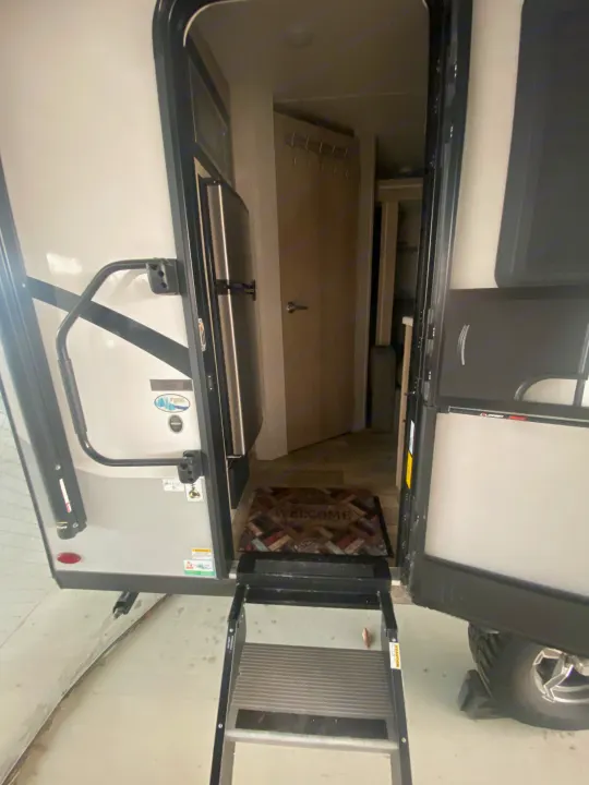 View inside an RV rental showing the entry steps, open main door, interior with a welcome mat, refrigerator, and hallway.. Forest River Flagstaff E-Pro 2022
