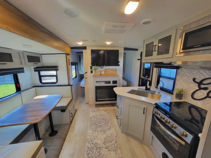 Spacious, modern RV rental interior featuring dining booth, kitchen, living area with TV & fireplace, and glimpse of bedroom.. Heartland RVs North Trail 2023