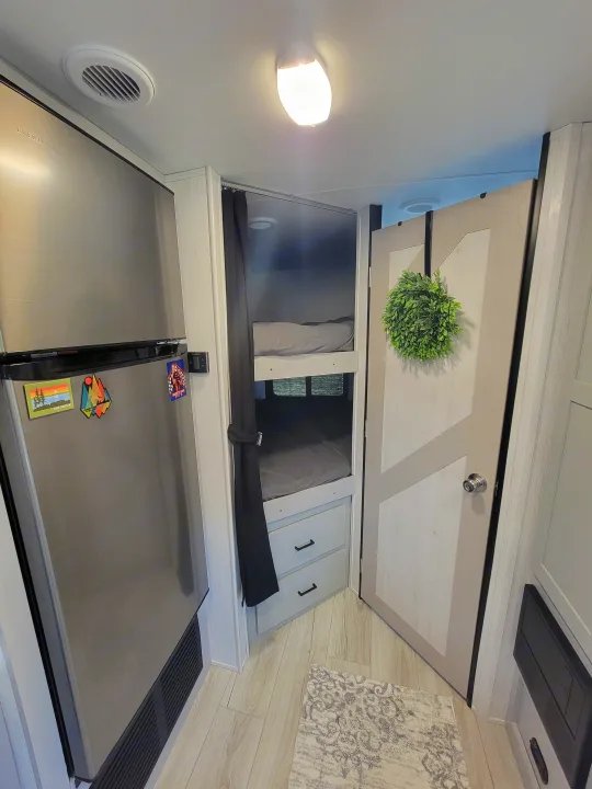 Cozy RV rental interior featuring bunk beds, a stainless steel fridge, and a door with a decorative wreath. Perfect for travel!. Heartland RVs North Trail 2023