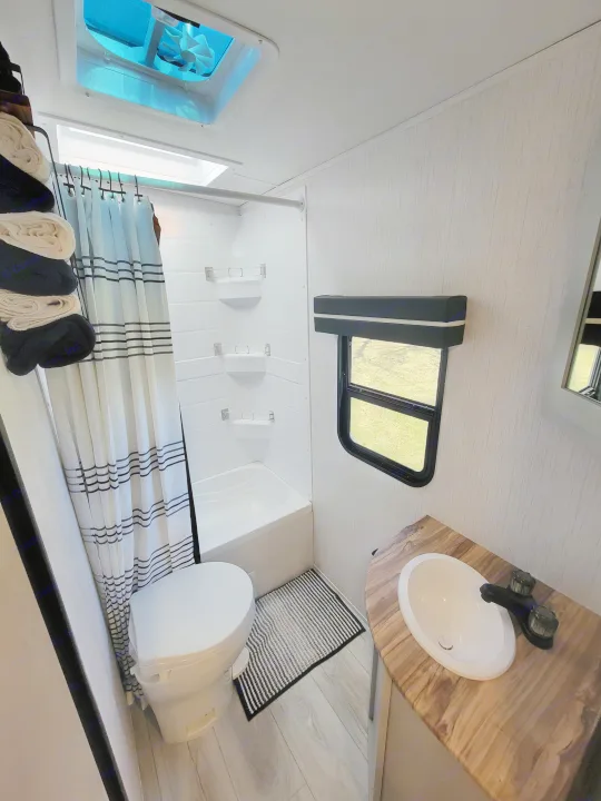 Clean RV rental bathroom interior, featuring a shower/tub, toilet, sink with wood-look counter, and window.. Heartland RVs North Trail 2023
