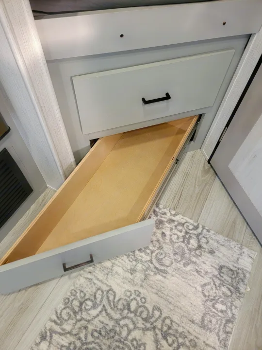 RV rental interior: Light grey drawers with black handles (one open, wood interior) on patterned rug.. Heartland RVs North Trail 2023