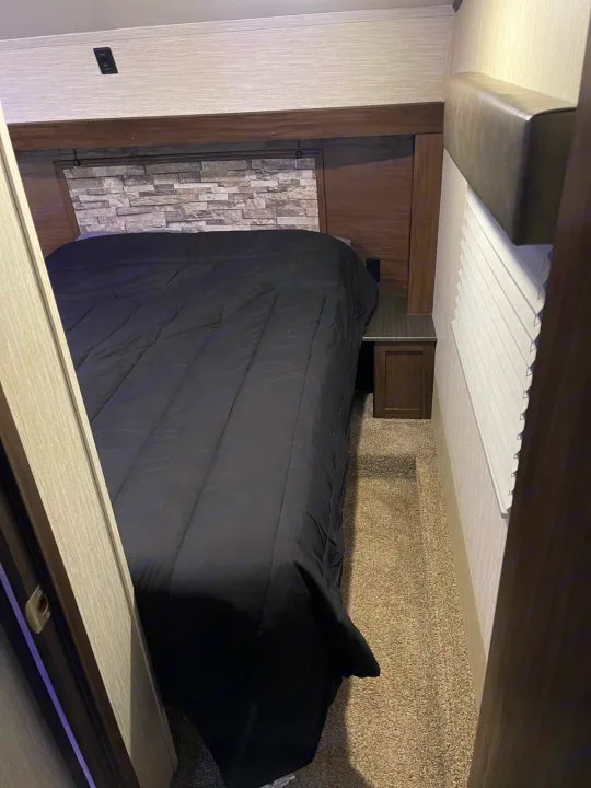 Cozy RV rental bedroom with a black comforter, stone headboard, and compact layout, ideal for travel adventures.. Forest River Cherokee Arctic Wolf 2019