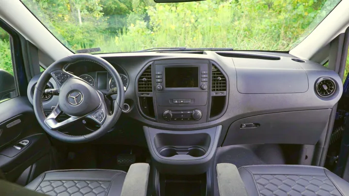 Interior of a Mercedes-Benz RV rental showing the dashboard, steering wheel with controls, central display, and front seats.. Mercedes-Benz Metris 2023