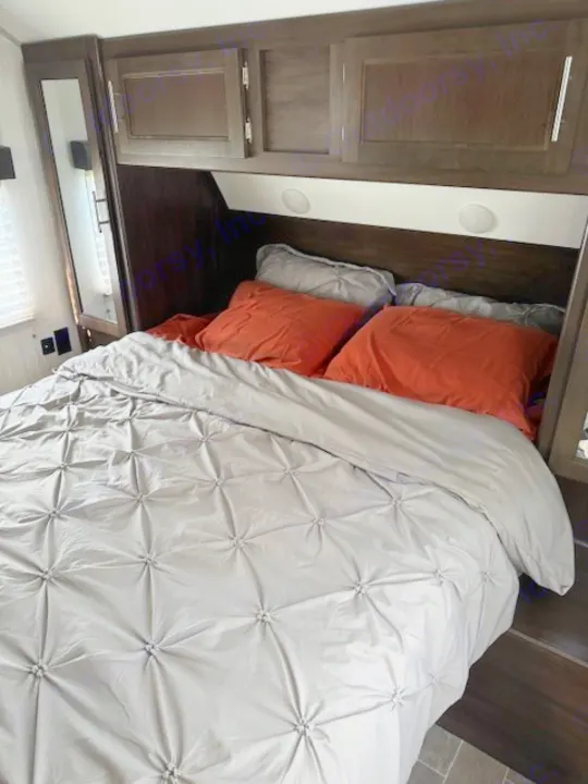 RV rental's inviting bedroom features a comfortable bed with a gray comforter, orange pillows, and overhead cabinets.. Forest River Cherokee Grey Wolf 2020