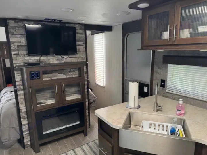 RV rental interior: modern living space with TV, fireplace, and kitchen area featuring an apron sink. Cozy and well-equipped.. Forest River Cherokee Grey Wolf 2020