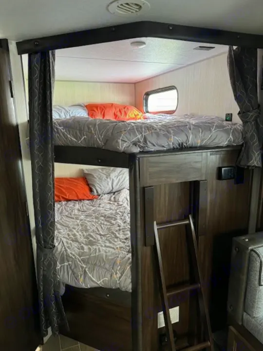RV rental: A cozy bunk bed setup inside, featuring two beds with grey bedding, a window on the top bunk, and a wooden ladder.. Forest River Cherokee Grey Wolf 2020