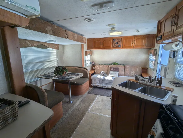 This RV rental interior shows a dining booth, sofa with a dog, and kitchen with sink, offering a homey travel experience.. Keystone RV Zeppelin Z-II 2006