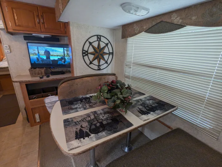 RV rental interior shows a dining area with table, banquette, TV, and compass. A cozy living space for travel.. Keystone RV Zeppelin Z-II 2006