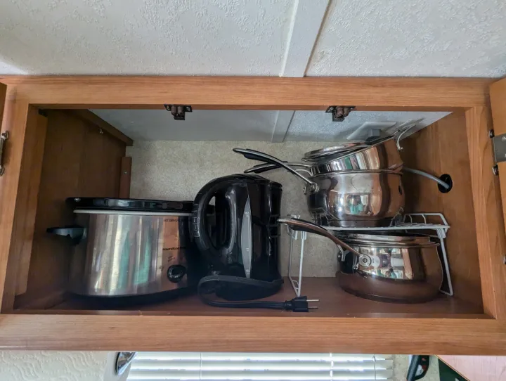 Inside an RV rental kitchen cabinet: slow cooker, electric kettle, and stacked pots/pans on a rack.. Keystone RV Zeppelin Z-II 2006