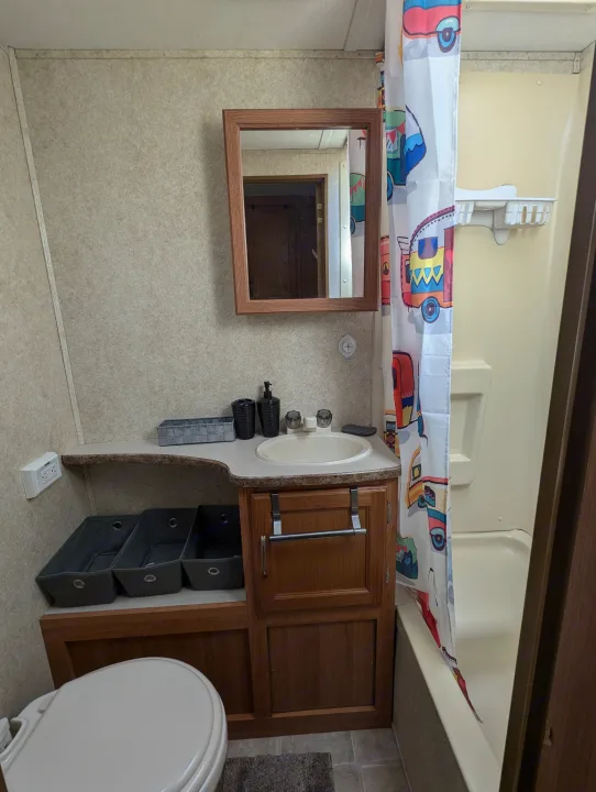 Compact RV rental bathroom with a tub/shower, vanity sink, toilet, and colorful shower curtain.. Keystone RV Zeppelin Z-II 2006