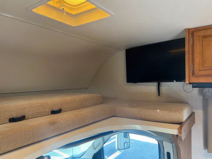 RV rental interior showing the over-cab bunk bed with cushions, a wall-mounted TV, and a ceiling vent.. Winnebago Minnie Winnie 2017