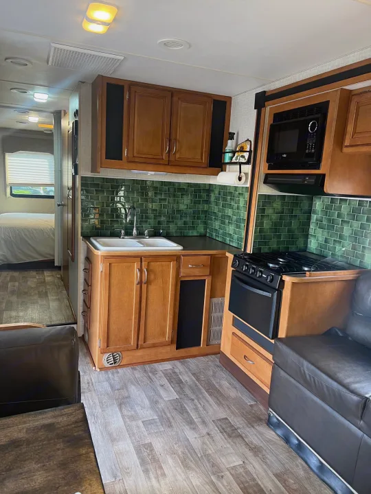 RV rental interior showcasing a modern kitchen with green tile, sink, stove, and microwave, plus a connected bedroom.. Winnebago Minnie Winnie 2017
