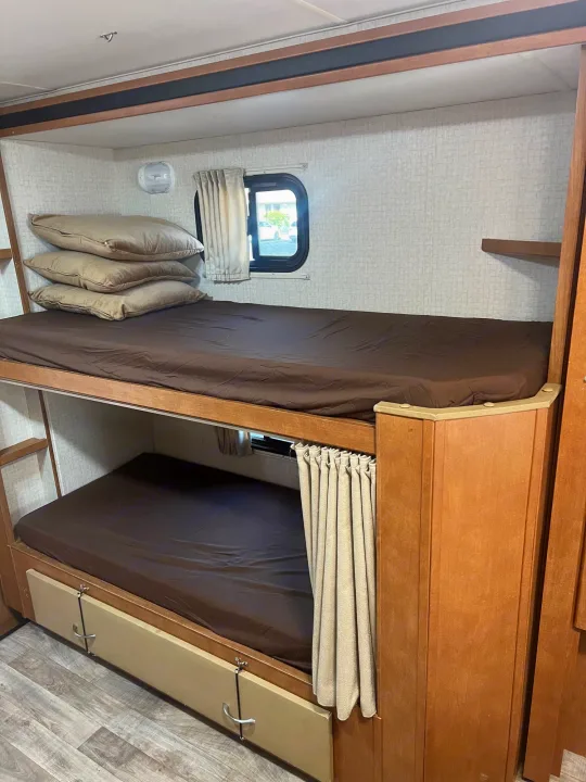 RV rental interior: Bunk beds with brown sheets, a window, and storage drawers for compact sleeping and living.. Winnebago Minnie Winnie 2017
