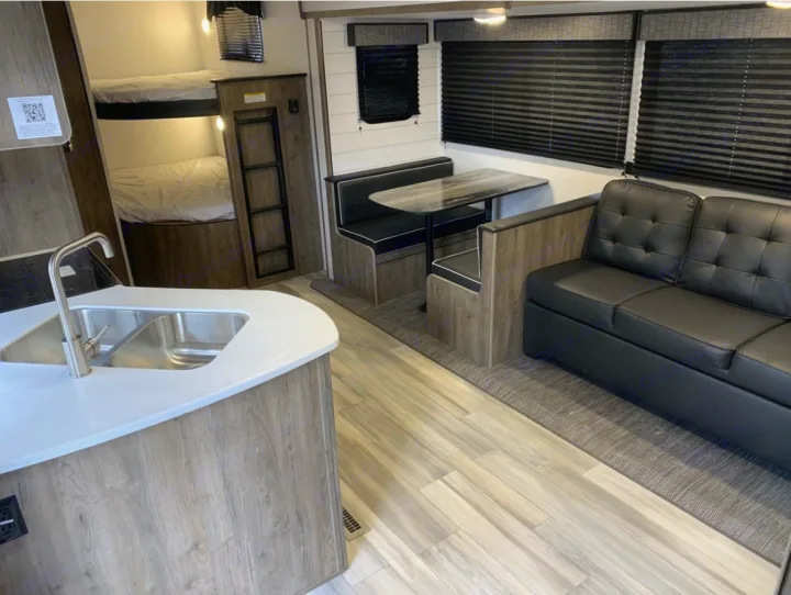 Modern RV rental interior featuring a kitchen island, dinette, bunk beds, and a black sofa for comfortable travel.. Pioneer Other 2023