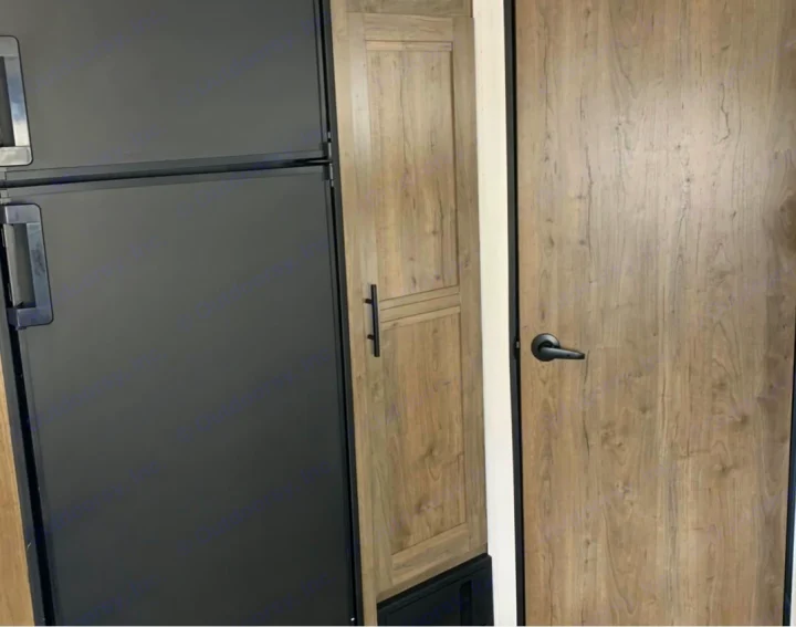 RV rental interior view: black refrigerator, light wood-grain cabinet, and door with black lever handle.. Pioneer Other 2023