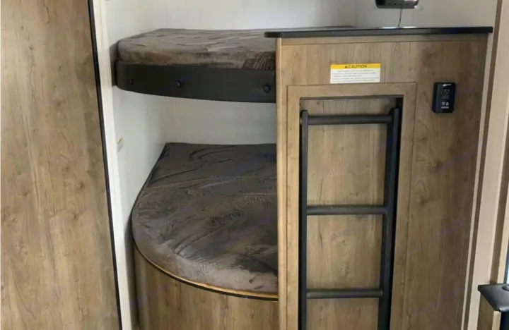 RV rental interior shows compact bunk beds with dark mattresses, a ladder, and a control panel.. Pioneer Other 2023