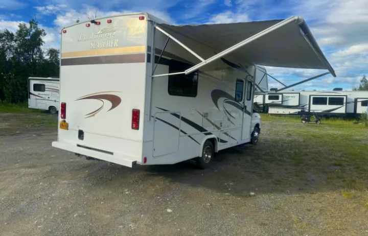 An RV rental, a Jamboree Searcher motorhome, showcasing its extended awning, parked in a sunny outdoor lot.. Jamboree Searcher 2014