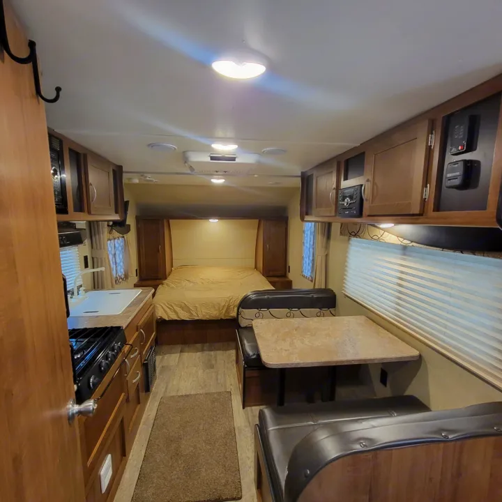 Interior view of an RV rental, featuring a bedroom, kitchenette with sink/stove, and dining area with bench seating.. Gulf Stream Ameri-Lite 2018