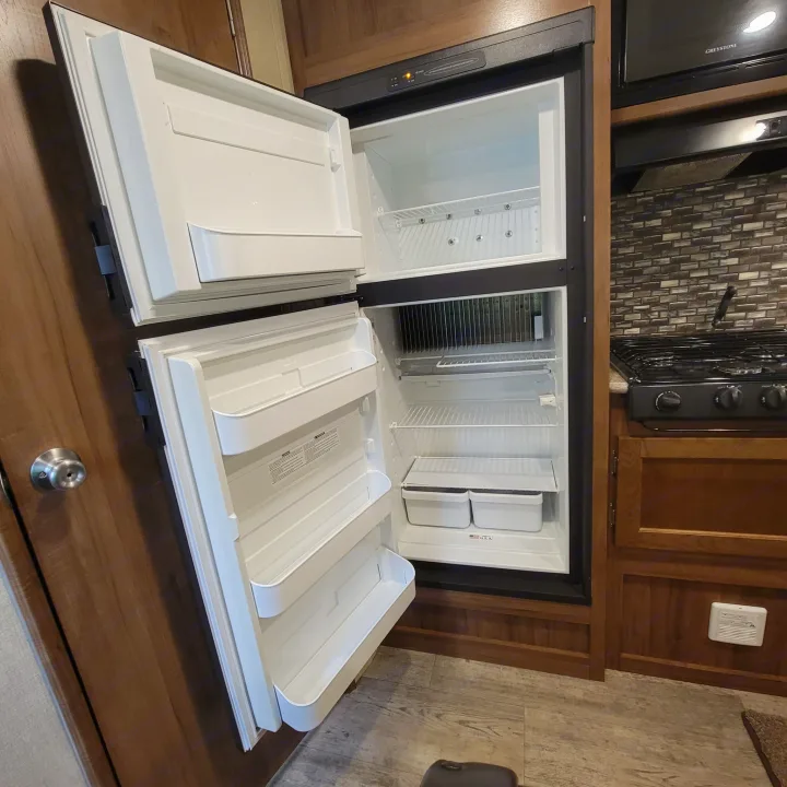 Open RV refrigerator and freezer in a compact kitchen area of an rv rental, ready for your trip's provisions.. Gulf Stream Ameri-Lite 2018