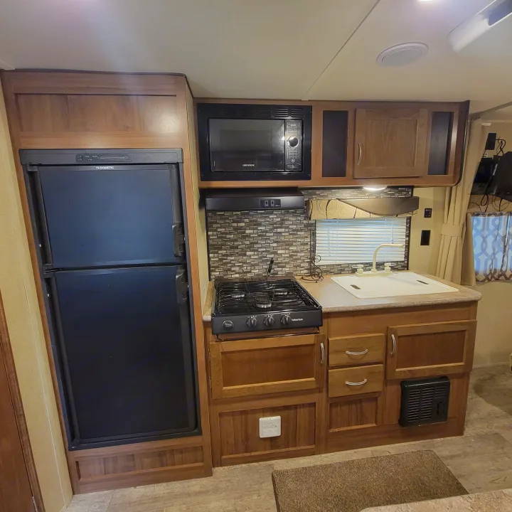 Efficient RV rental kitchen featuring a refrigerator, microwave, stove, and sink, ideal for preparing meals on the go.. Gulf Stream Ameri-Lite 2018