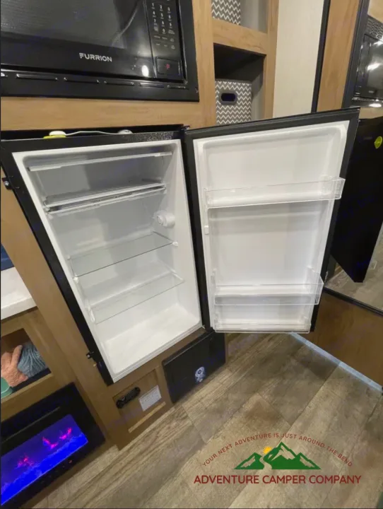 Compact RV rental interior featuring a Furrion microwave, an open mini-fridge, and cozy living space, ideal for camping adventures.. Forest River Cherokee Wolf Pup 2024