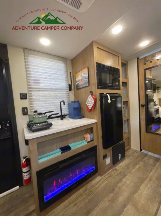 Compact RV rental interior: kitchen with microwave, fridge, sink, and an electric fireplace. Ideal for your next journey.. Forest River Cherokee Wolf Pup 2024