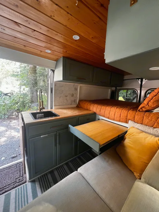 RV rental interior: cozy bed, compact kitchen with pull-out table, and comfy living area. Ideal for van life.. Dodge Promaster 2500 2023