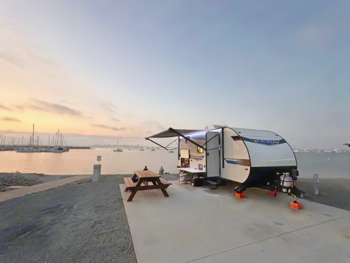 Peaceful waterfront sunset with an RV rental. A travel trailer is parked by the bay with boats & a picnic table.. Forest River Salem FSX Plantium 2022