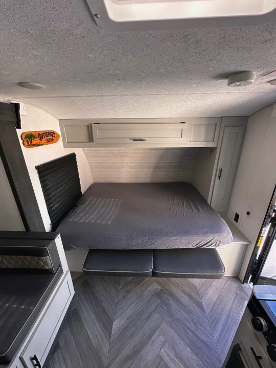 Interior of an rv rental camper: grey bed, sleek overhead cabinets, and a chevron wood floor. A compact, functional space.. Forest River Salem FSX Plantium 2022