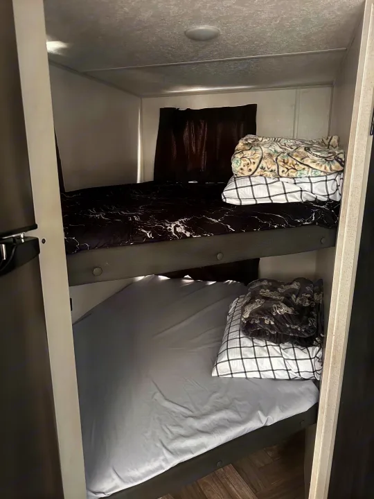 This RV rental features stacked bunk beds, providing compact sleeping space. The top bunk has patterned bedding, while the bottom has a light sheet.. Forest River Salem FSX Plantium 2022