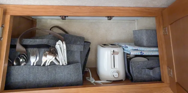 Organized RV rental kitchen cabinet with a felt caddy holding silverware, a white toaster, and dishes in storage bins.. Keystone RV Zeppelin Z-II 2006