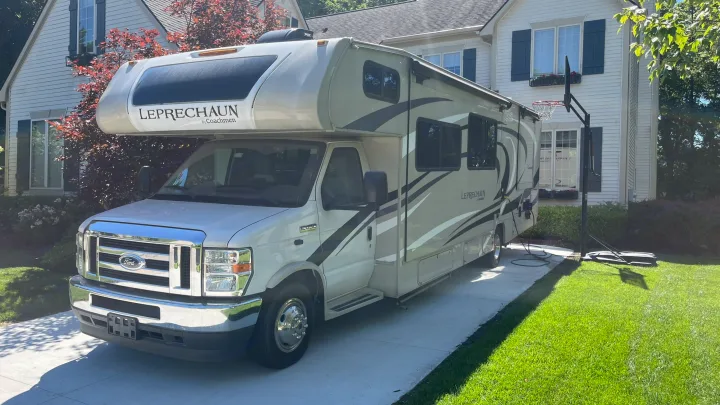 A light-colored Coachmen Leprechaun Class C motorhome RV rental parked on a sunny residential driveway.. Coachmen Leprechaun 2021