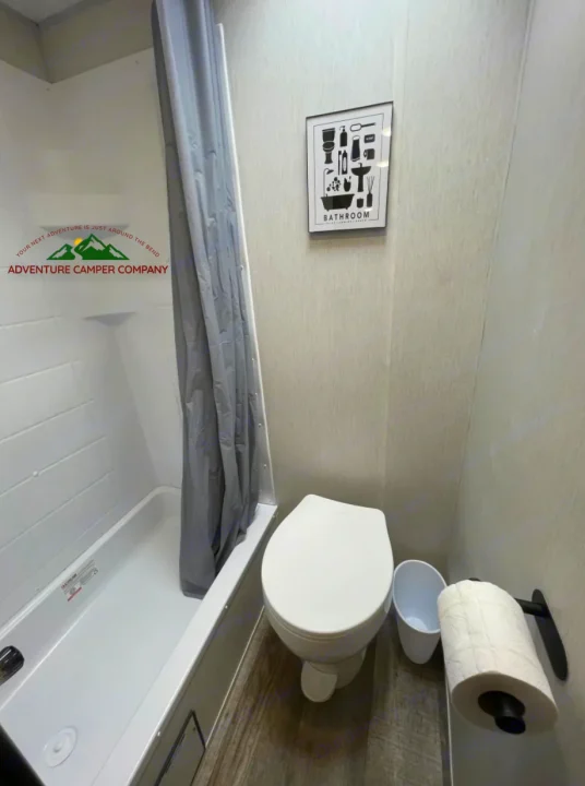 RV rental bathroom: A clean, compact space with a white shower/tub, gray curtain, toilet, and decorative wall art.. Forest River Cherokee Wolf Pup 2024