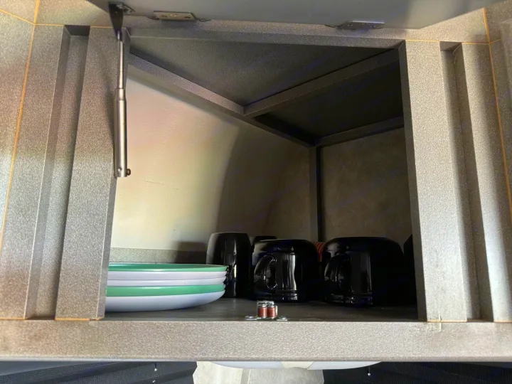 Inside an RV rental: a compact cabinet with plates & mugs, held open by a gas strut. Practical kitchen storage.. Weekend Warrior 1800sxfk 2009